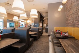 Un interior de restaurante con cabinas y mesas, iluminación colgante, paredes de ladrillo y una alfombra estampada.