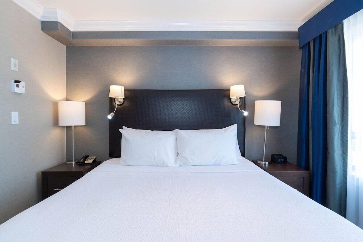 Une chambre d’hôtel avec un grand lit, deux tables de chevet, deux lampes fixées au mur, un téléphone et une horloge.