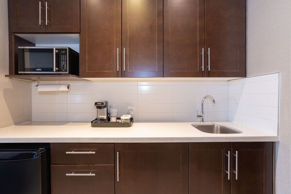 A kitchen with dark brown cabinets, a microwave, a coffee maker, and a sink. - Sandman Signature Edmonton South Hotel (Edmonton)
