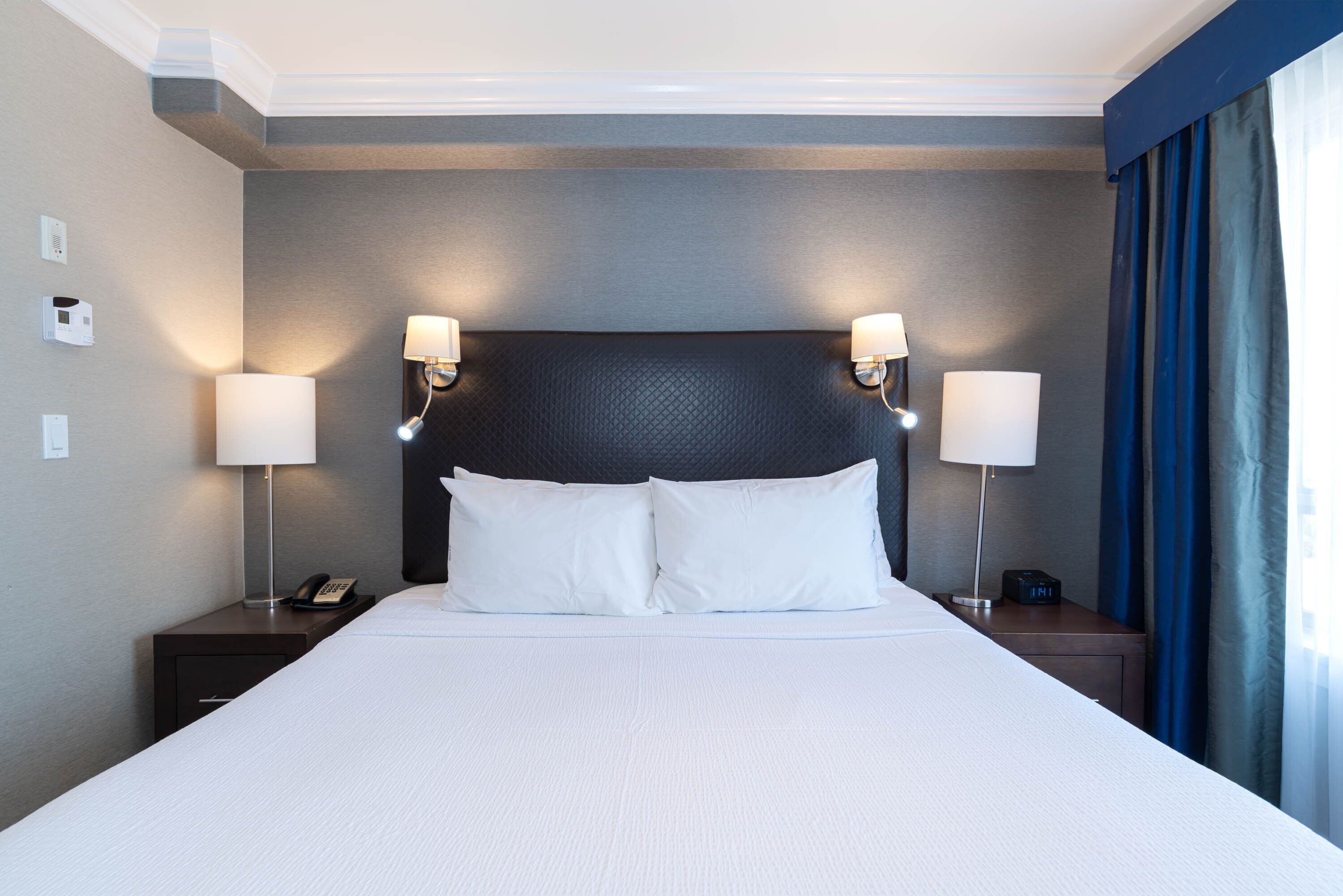 Une chambre d’hôtel avec un grand lit, deux tables de chevet avec des lampes, un téléphone et une horloge.