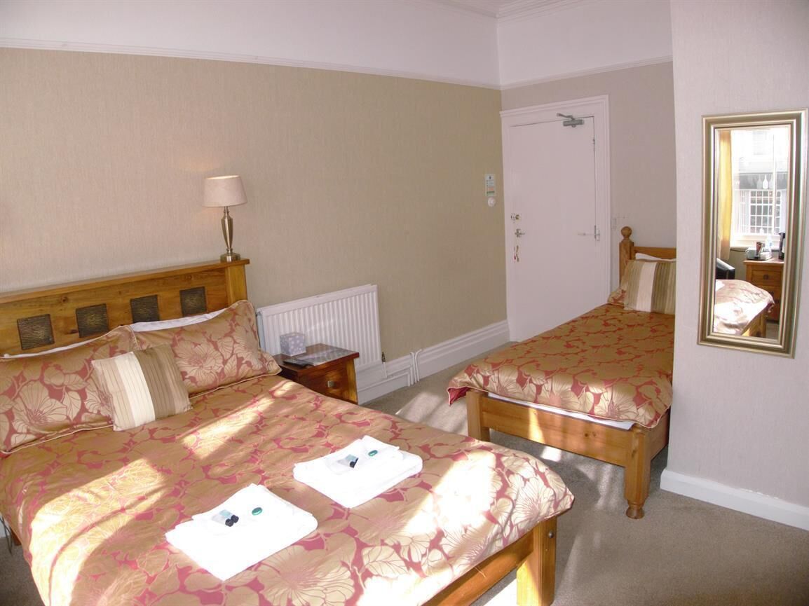 A hotel room with two single beds, a bedside table with a lamp, a radiator, and a door with a mirror.