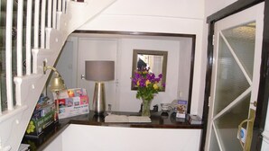 Un mostrador de recepción con una lámpara, un jarrón de flores y un folleto con 'Lugares para visitar'.