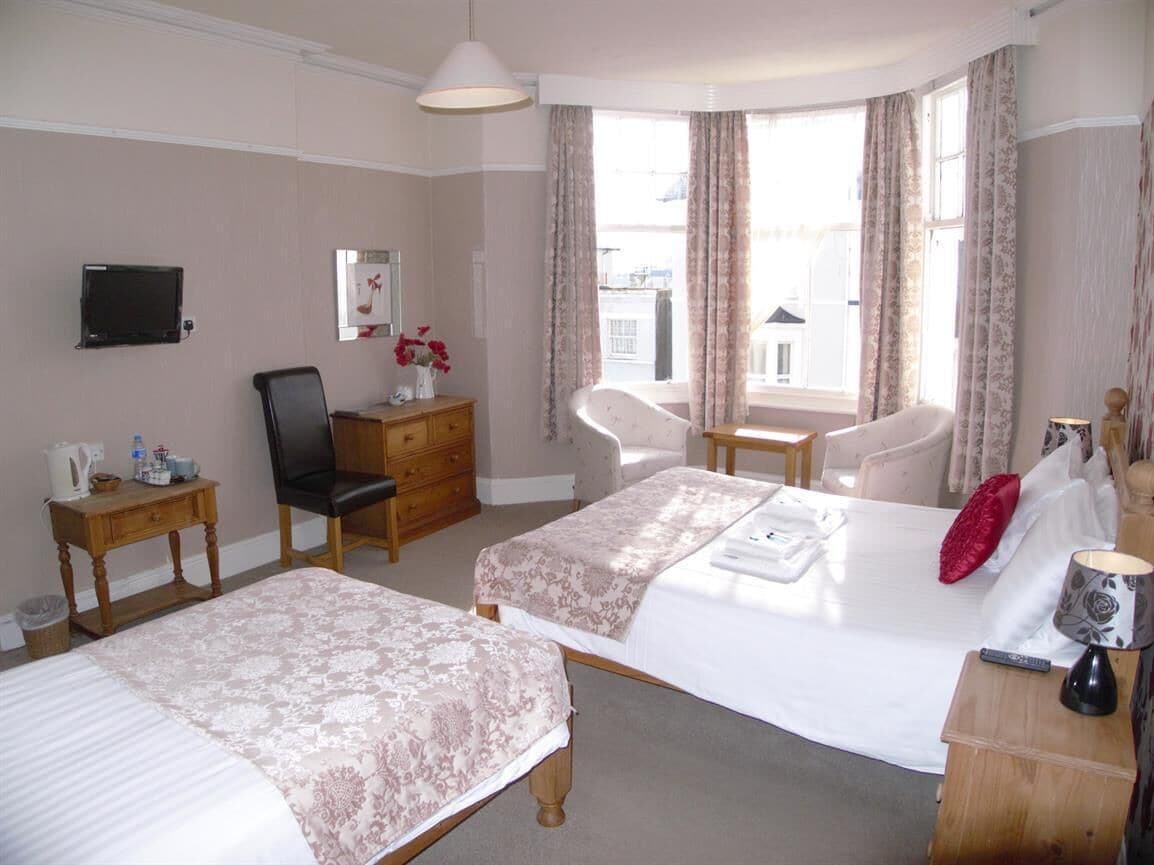 A hotel room with two beds, a desk, a chair, a television, and a window with curtains.