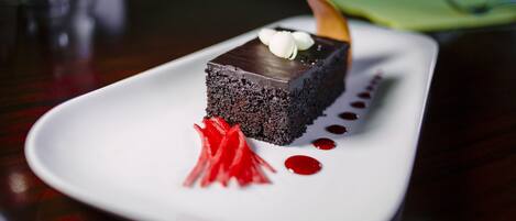 Un postre sobre un plato blanco, con base de chocolate, cobertura de crema blanca y un detalle decorativo encima.