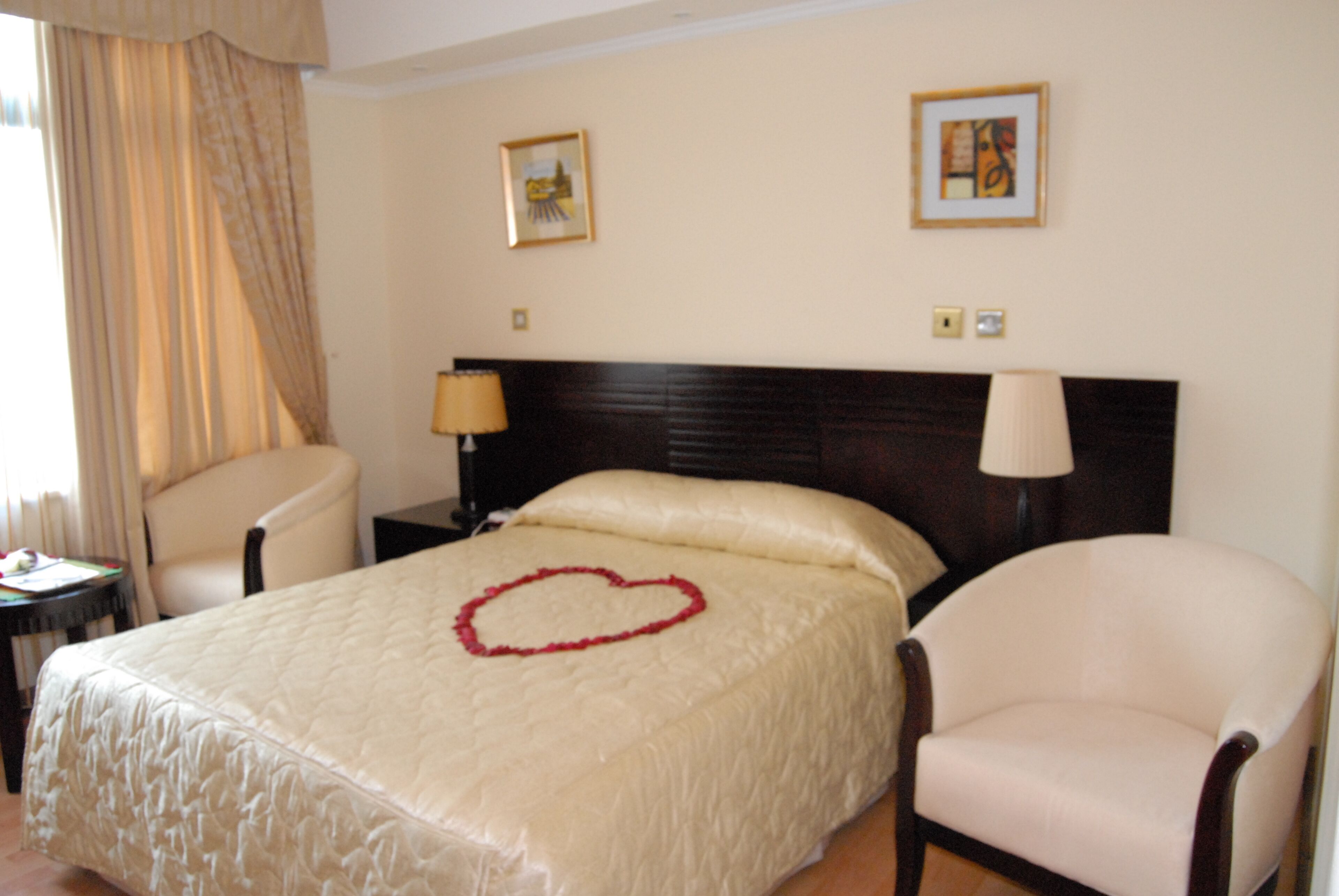 A hotel room with a large bed, two chairs, a nightstand with a lamp, and two framed pictures on the wall.