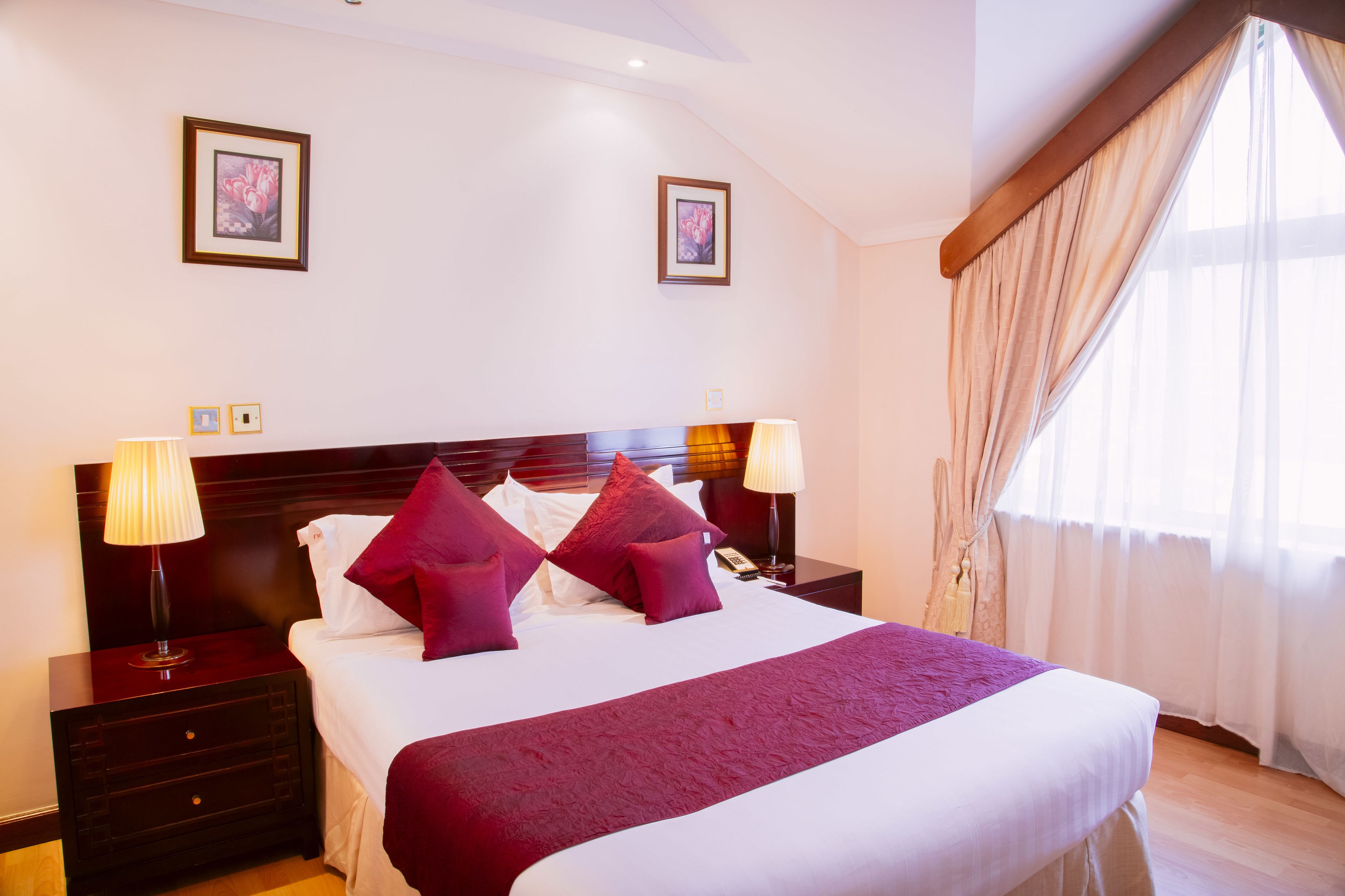 A hotel room with a large bed, two bedside tables with lamps, a wooden headboard, and two framed pictures on the wall.