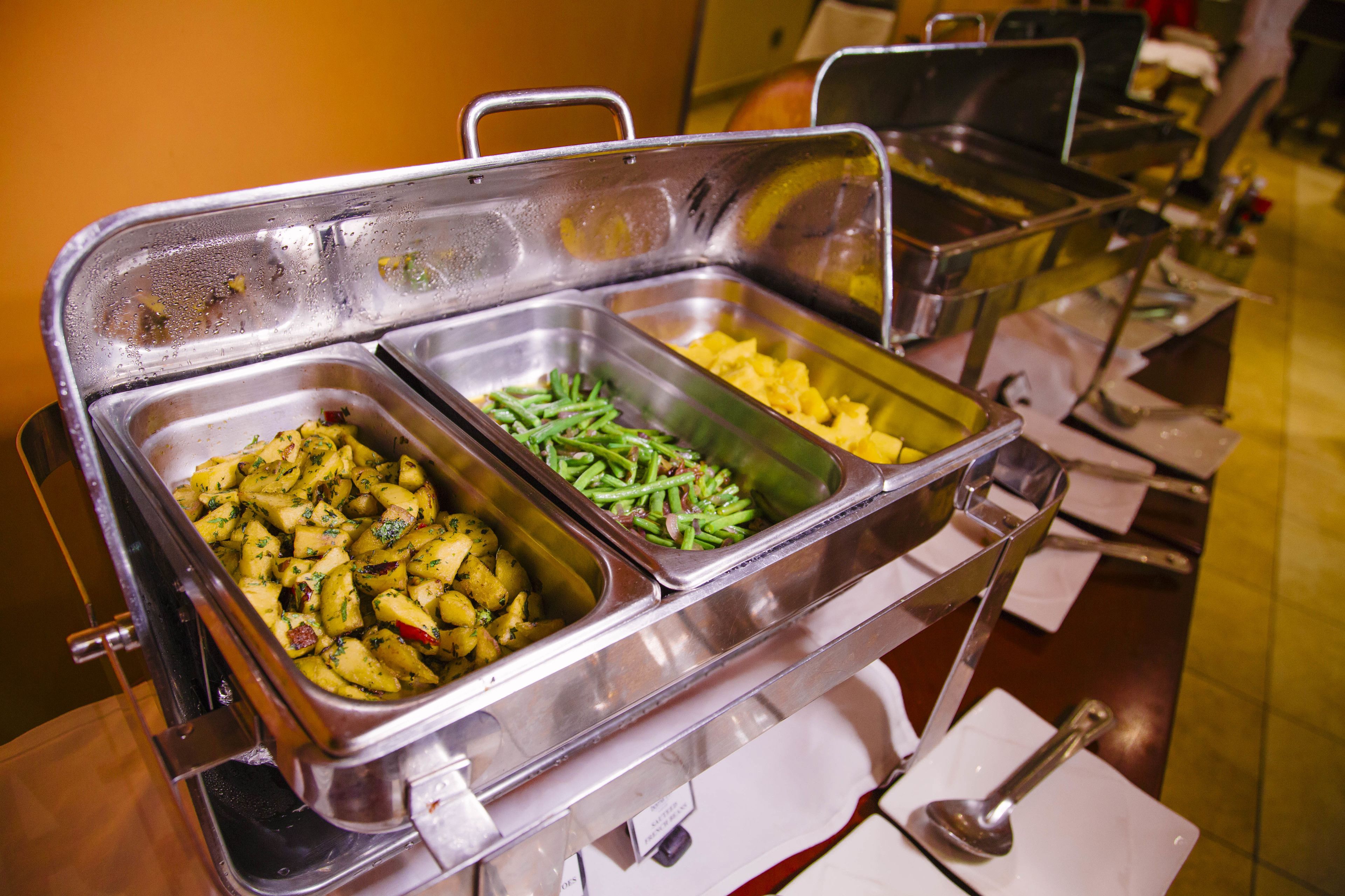 Een buffet met meerdere metalen opschepbakken vol met verschillende gerechten.