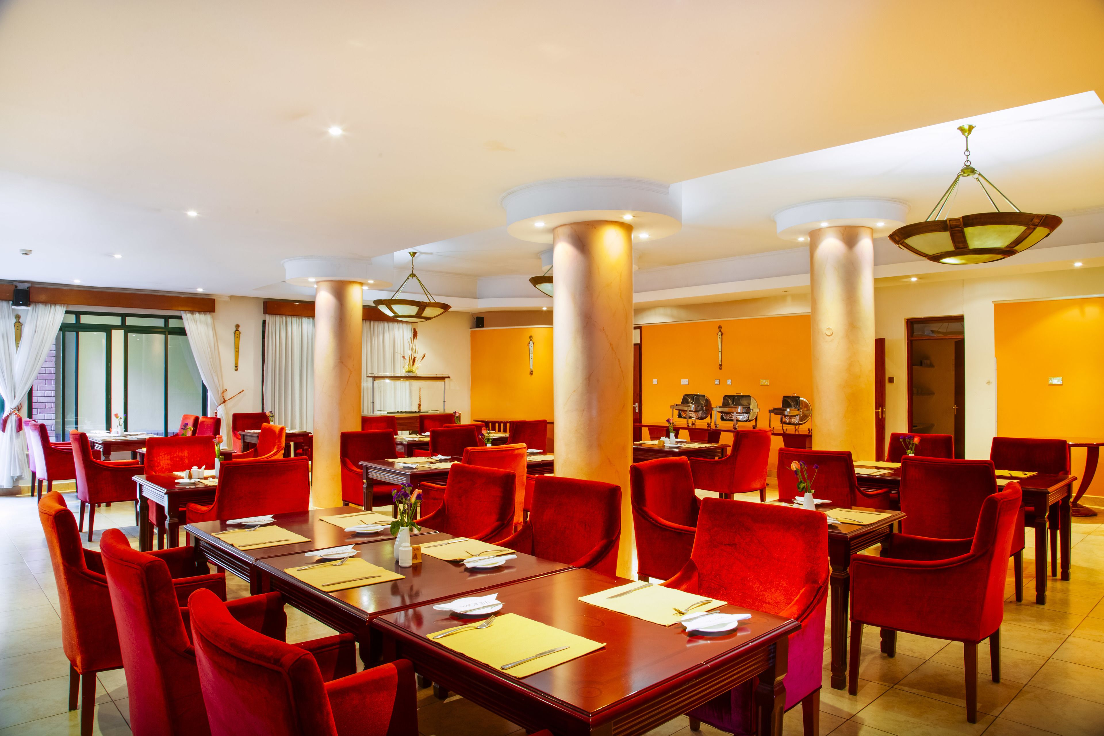 Un comedor de hotel con sillas rojas, mesas de madera y una lámpara de araña moderna.