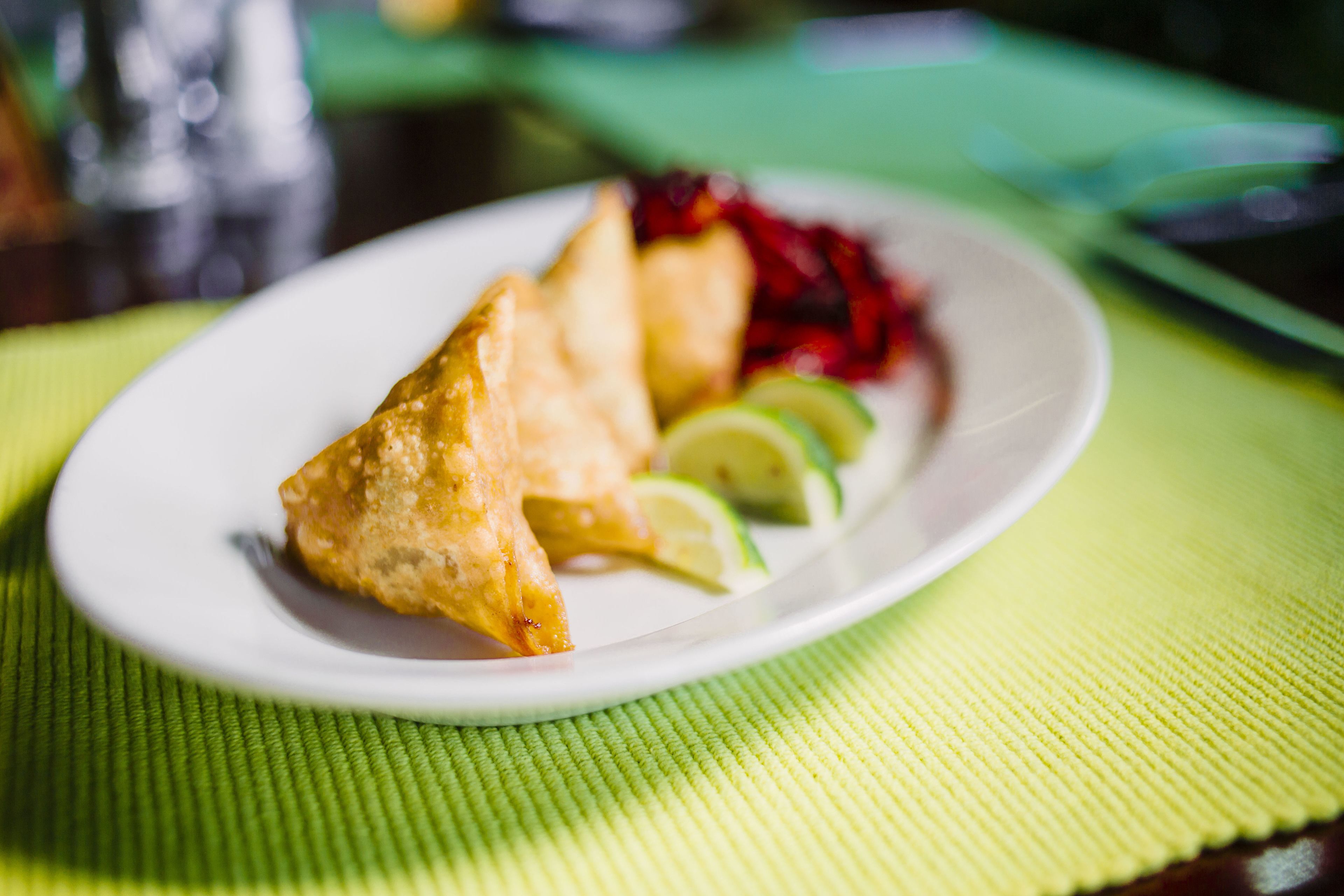 Um prato com um samosa, fatias de limão e um acompanhamento de beterraba em um prato branco.