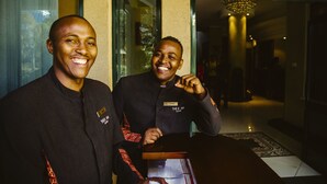 Two individuals standing in a hotel lobby with a chandelier and a patterned rug. - Boma Inn Nairobi (Nairobi)