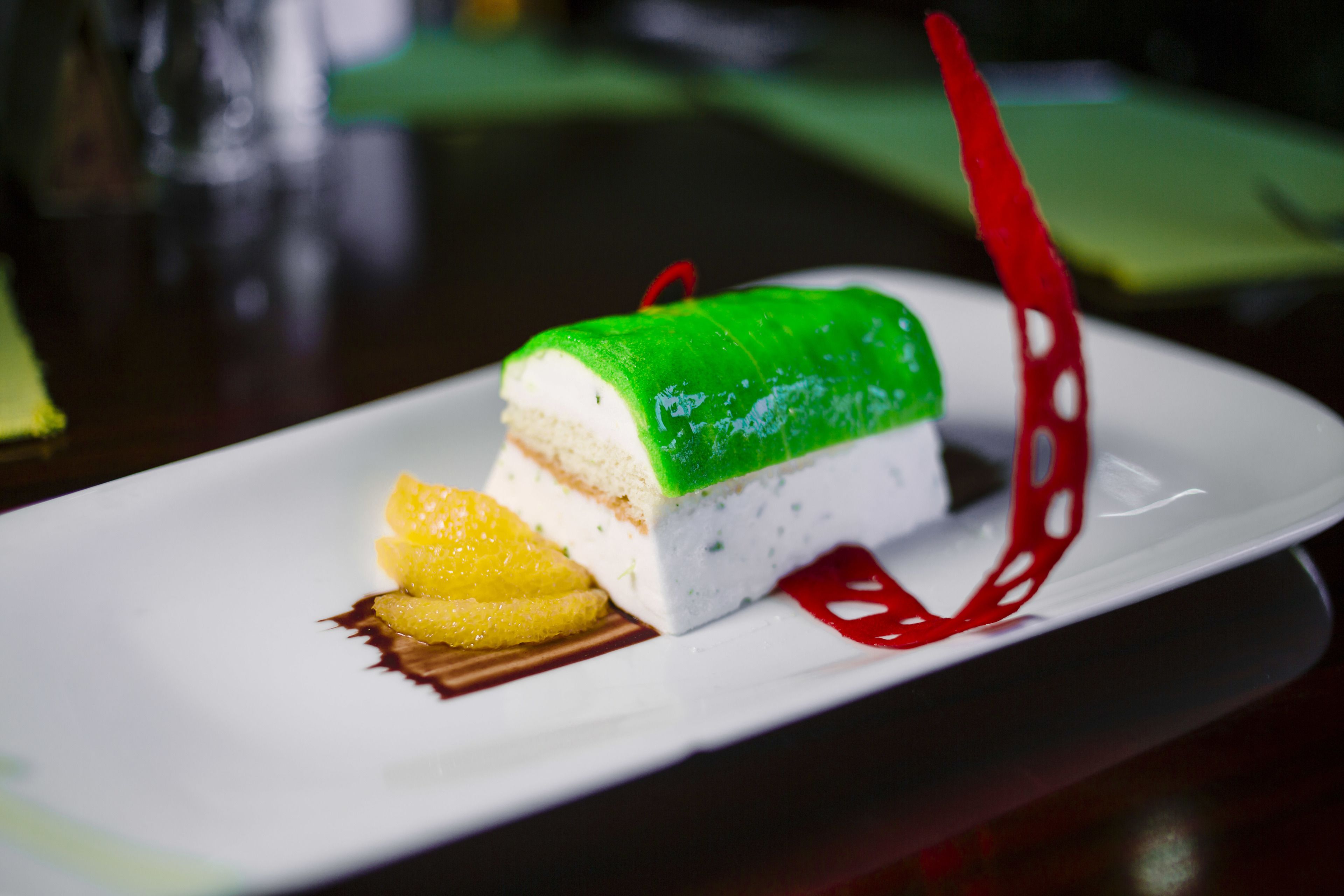 A dessert with a green top, white base, and a red decoration on a white plate.