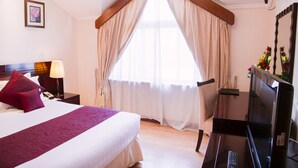 A hotel room with a large bed, a desk with a TV, and a window with curtains. - Boma Inn Nairobi (Nairobi)
