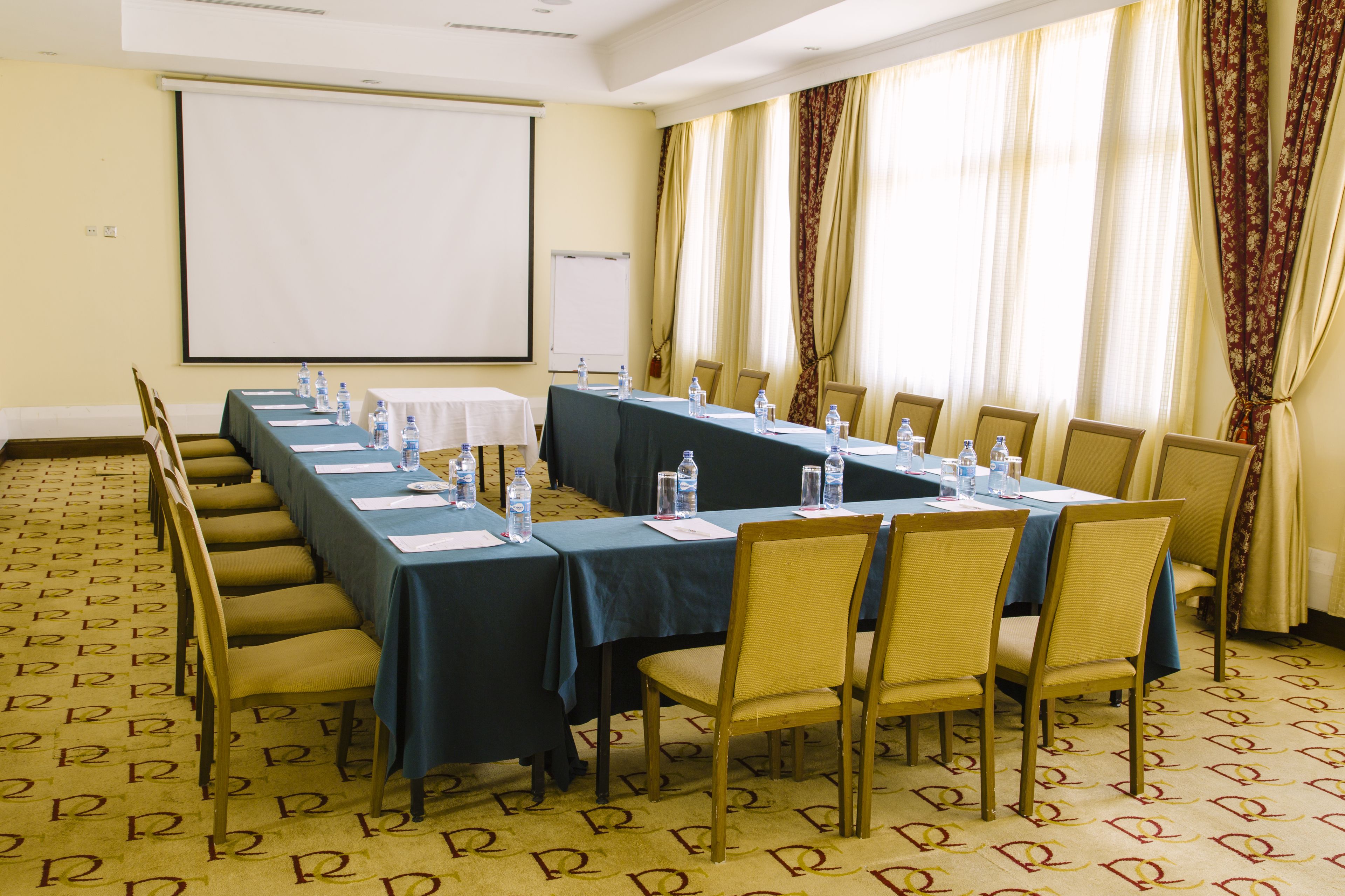 A conference room with a long table, chairs, water bottles, and a projector screen.