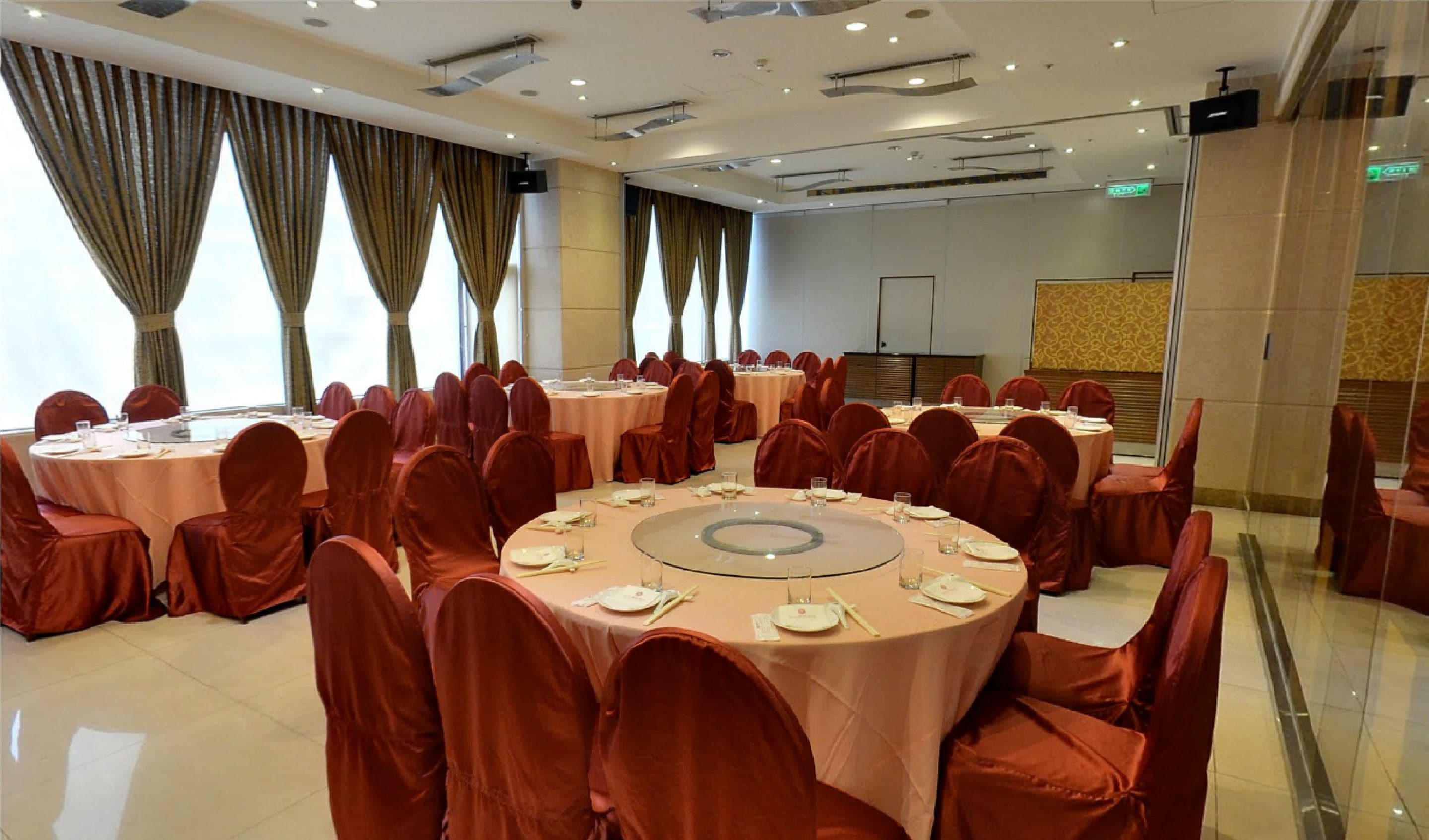 A conference room with round tables and chairs, large windows with curtains, and a modern ceiling with recessed lighting.