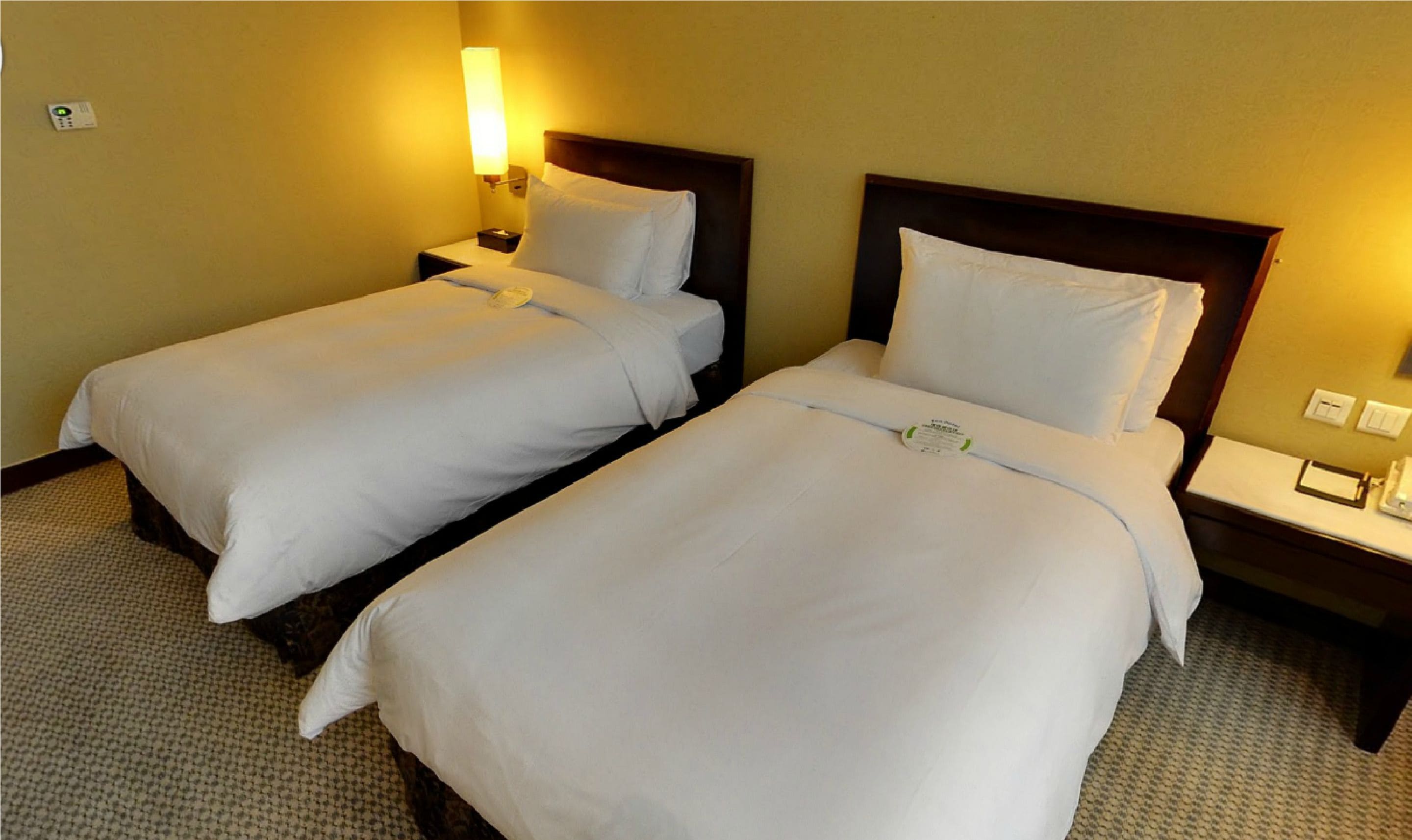 Una habitación de hotel con dos camas individuales, cada una con cabecera de madera, una mesita de noche y un buró.