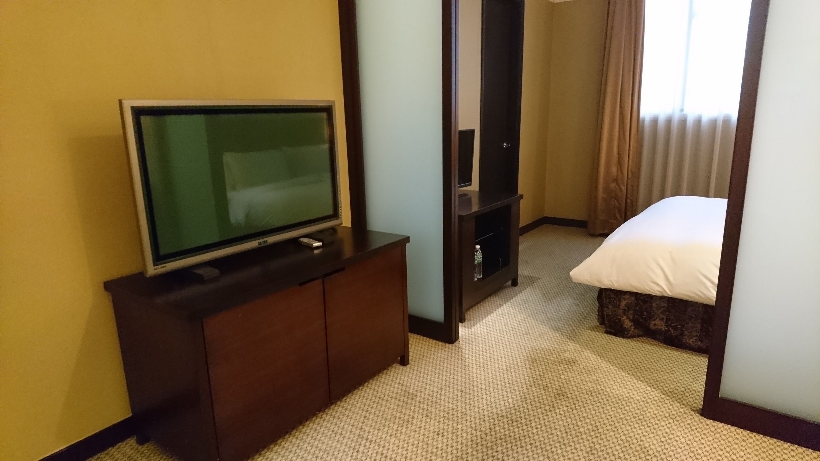 Una habitación de hotel con una cama, un televisor sobre un mueble de madera y un estante pequeño.