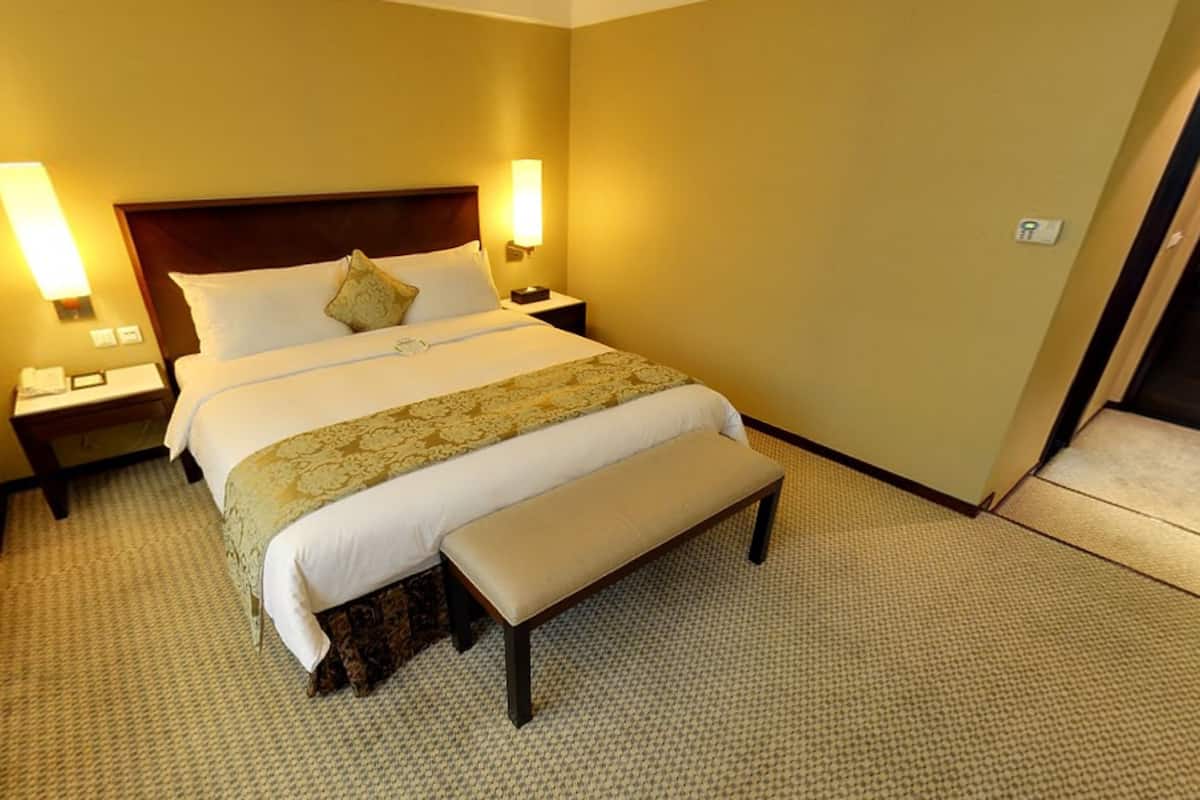 Une chambre d’hôtel avec un grand lit, une banquette, deux tables de chevet avec des lampes et un sol recouvert de moquette.