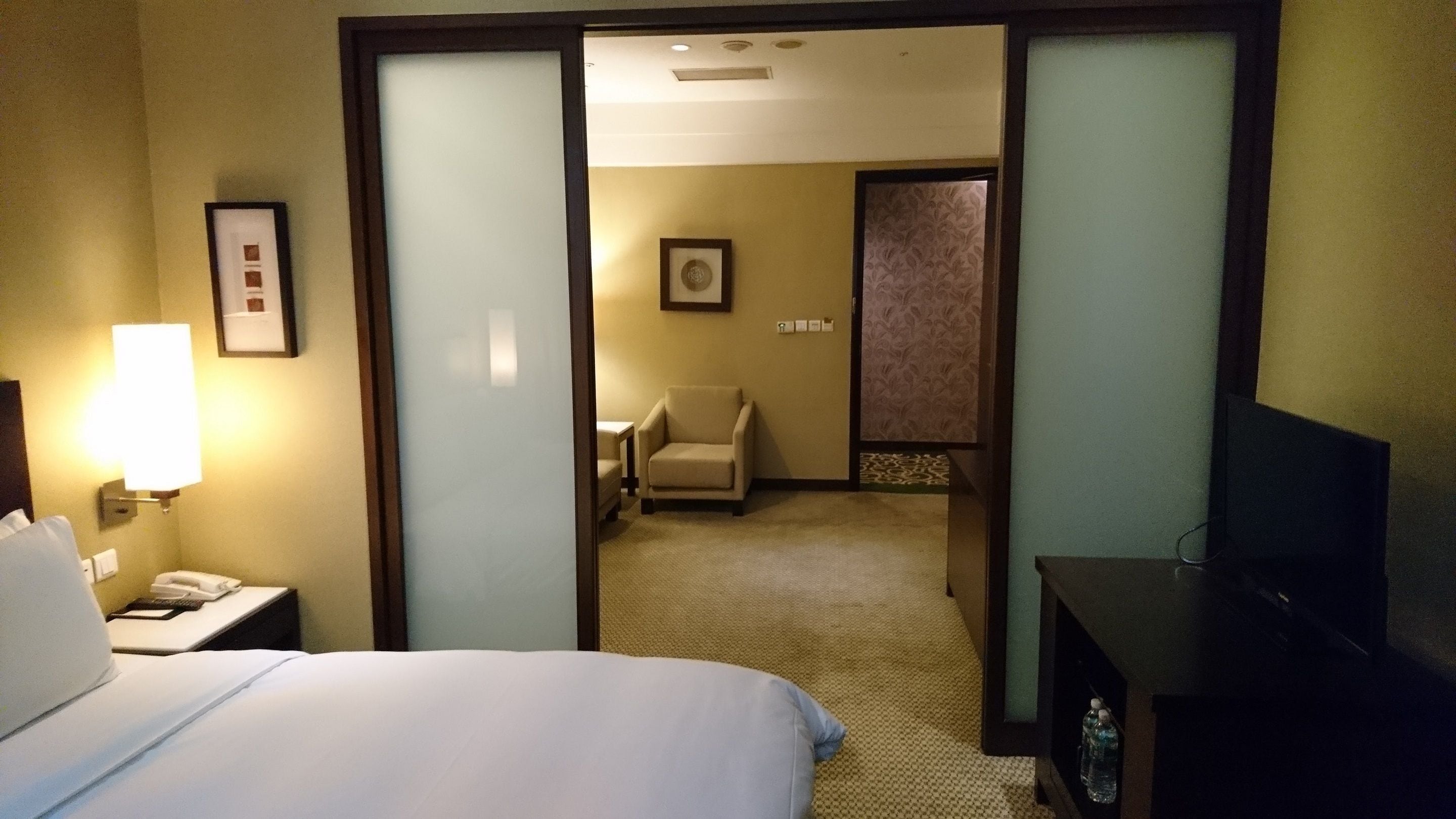Ein Hotelzimmer mit einem Bett, einem Schreibtisch mit Lampe, einem Sessel und einem Fernseher.