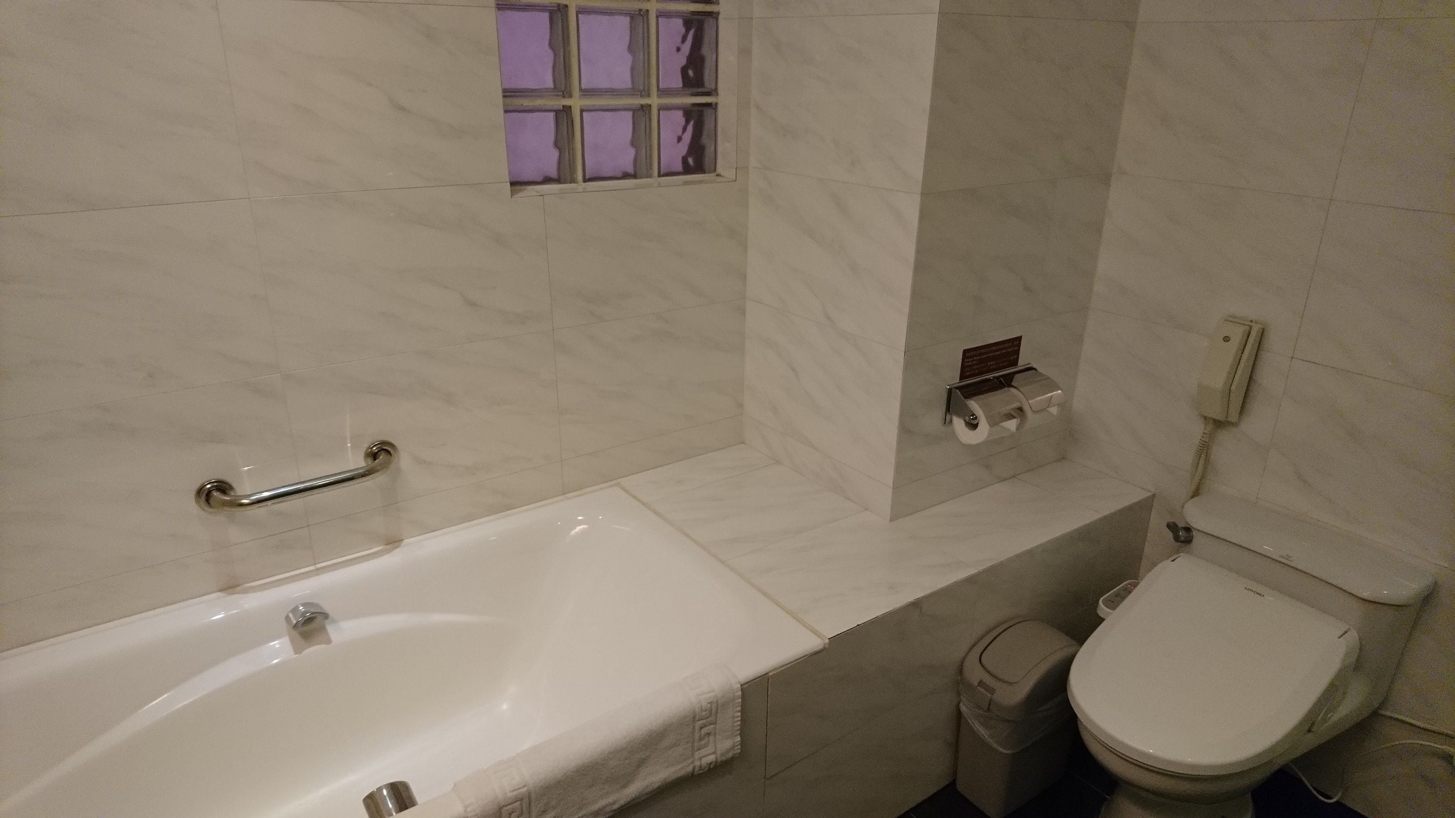 A bathroom with a bathtub, toilet, and a trash bin.