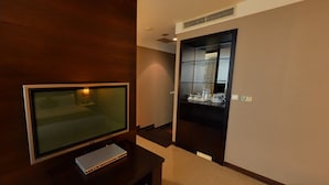 A modern hotel room with a large flat-screen TV on a wooden stand, a small side table, and a built-in kitchen area with a microwave and kettle. - Taipei International Hotel (Taipei)