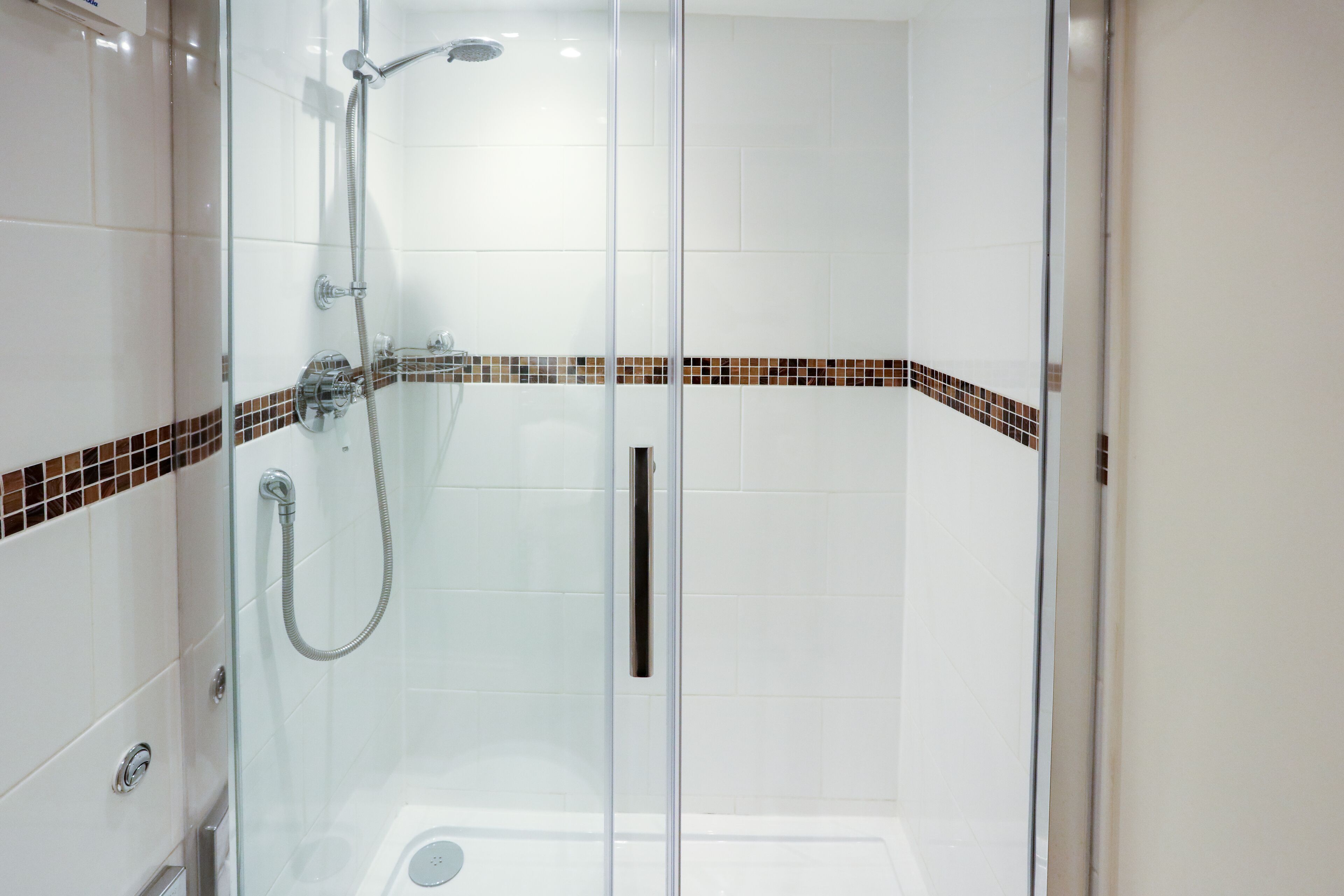 A glass-enclosed shower area with a tiled wall and a brown-tiled border.