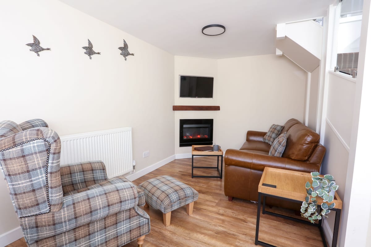 A living room with a fireplace, a brown leather sofa, a plaid armchair, and a small wooden table.