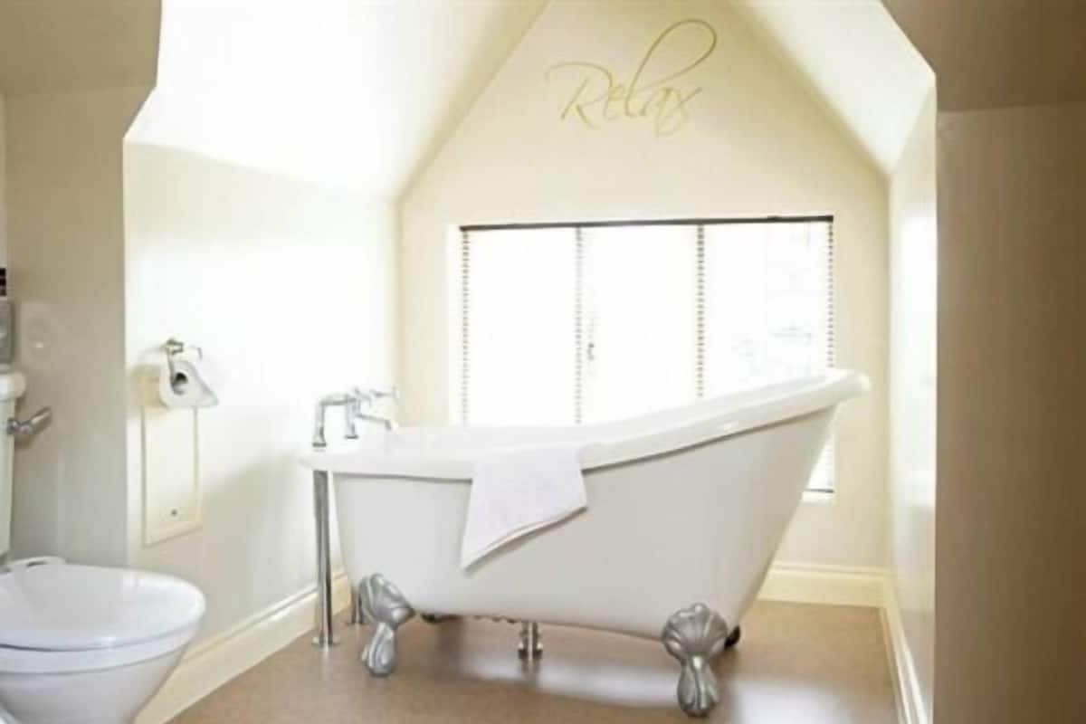 A bathroom with a freestanding bathtub, a toilet, and a window with blinds.