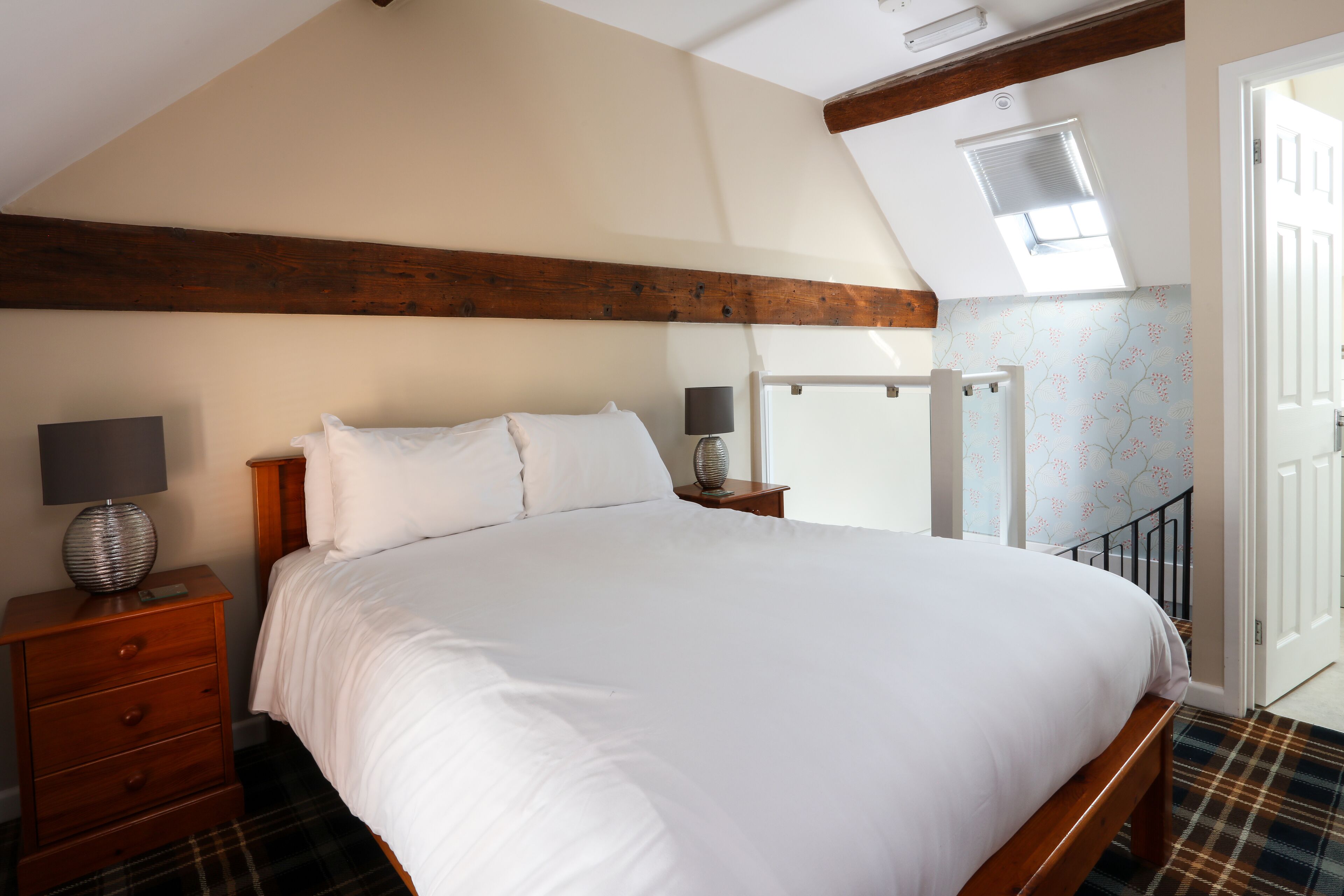 Un dormitorio con una cama grande, cabecera de madera, una mesita de noche con lámpara y una ventana con persianas.