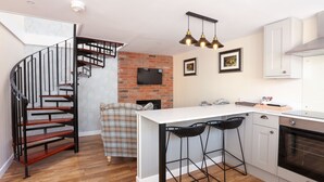 A modern kitchen with a white countertop, black bar stools, a brick wall, and a black spiral staircase. - Broom Hall Inn (Alcester)