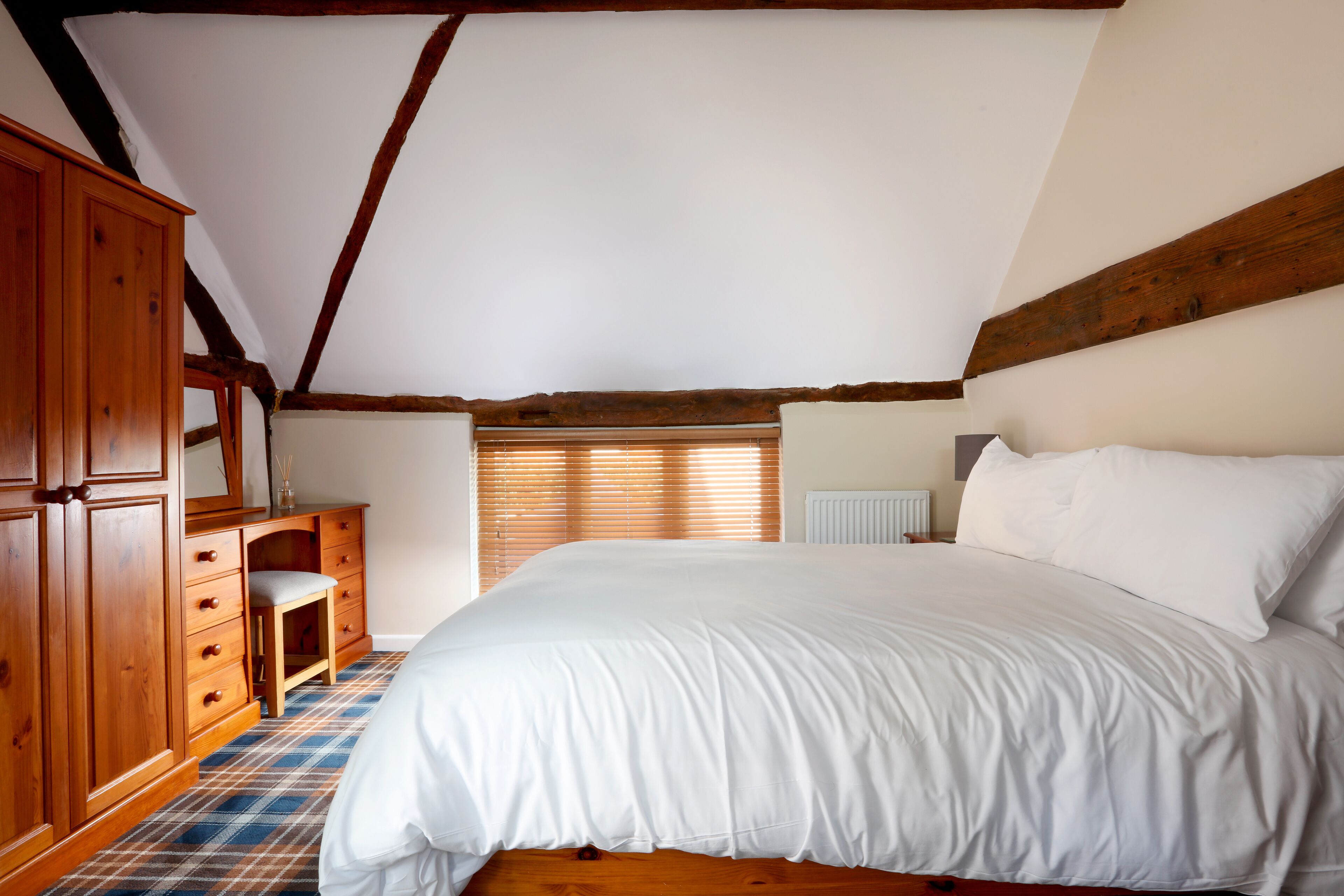 Un dormitorio con una cama grande, un armario de madera y una silla pequeña.