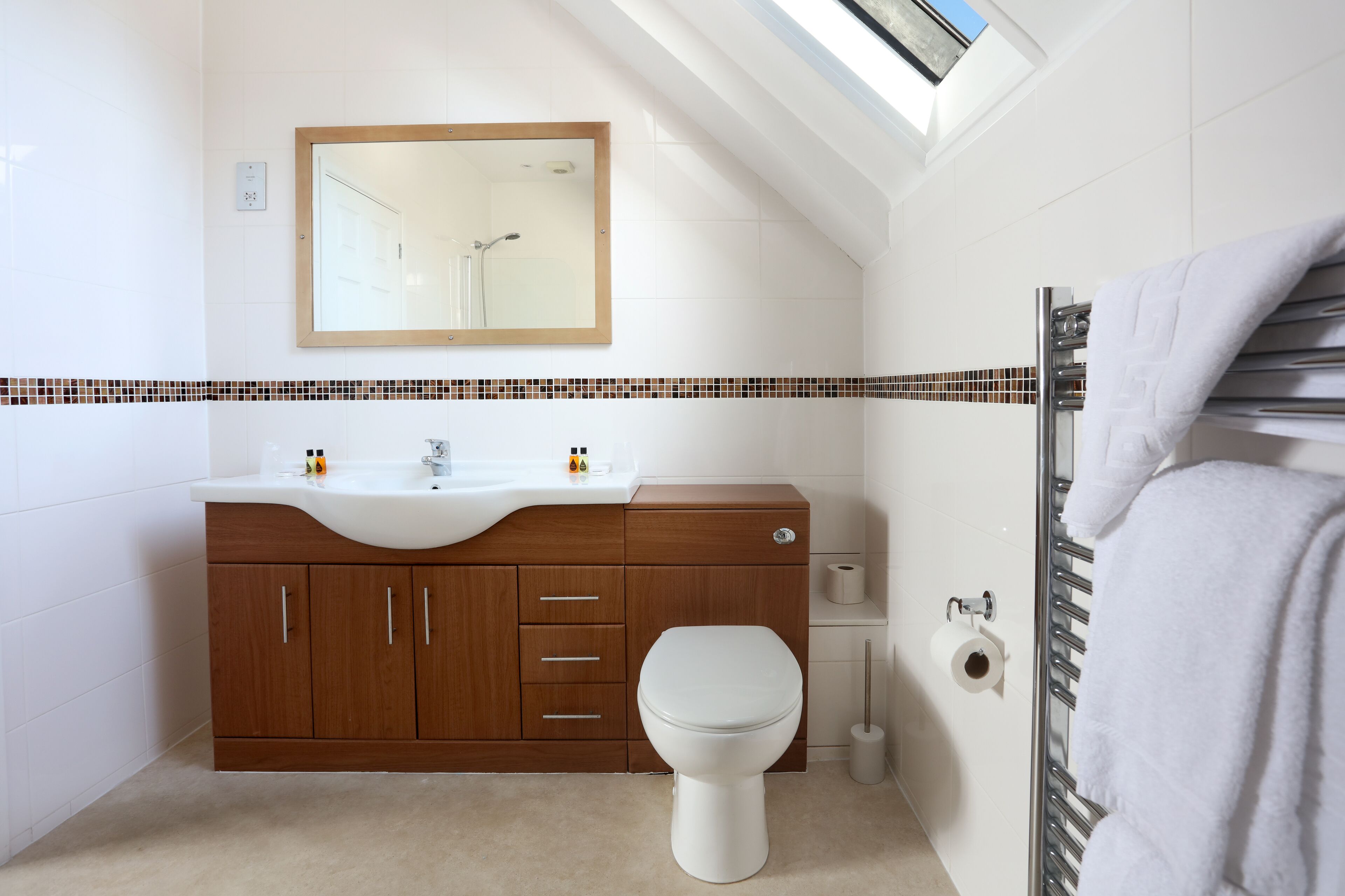Une salle de bain moderne avec un puits de lumière, un lavabo blanc, des meubles en bois et des toilettes.