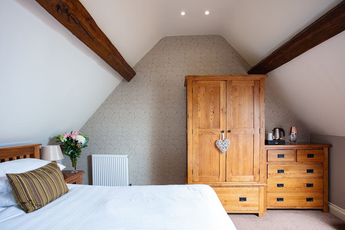 A bedroom with a large bed, a wooden wardrobe, a nightstand with a lamp, and a radiator.