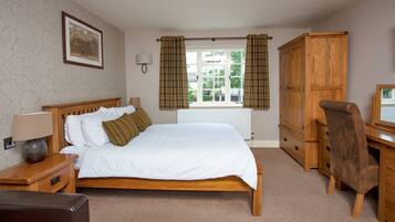 A bedroom with a wooden bed, a wooden desk, a chair, a lamp, and a window with curtains.