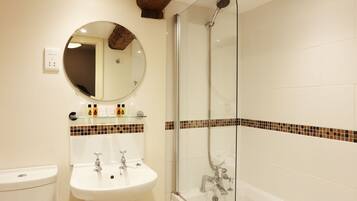 Un baño con ducha de mampara de vidrio, un espejo redondo y un lavabo blanco.