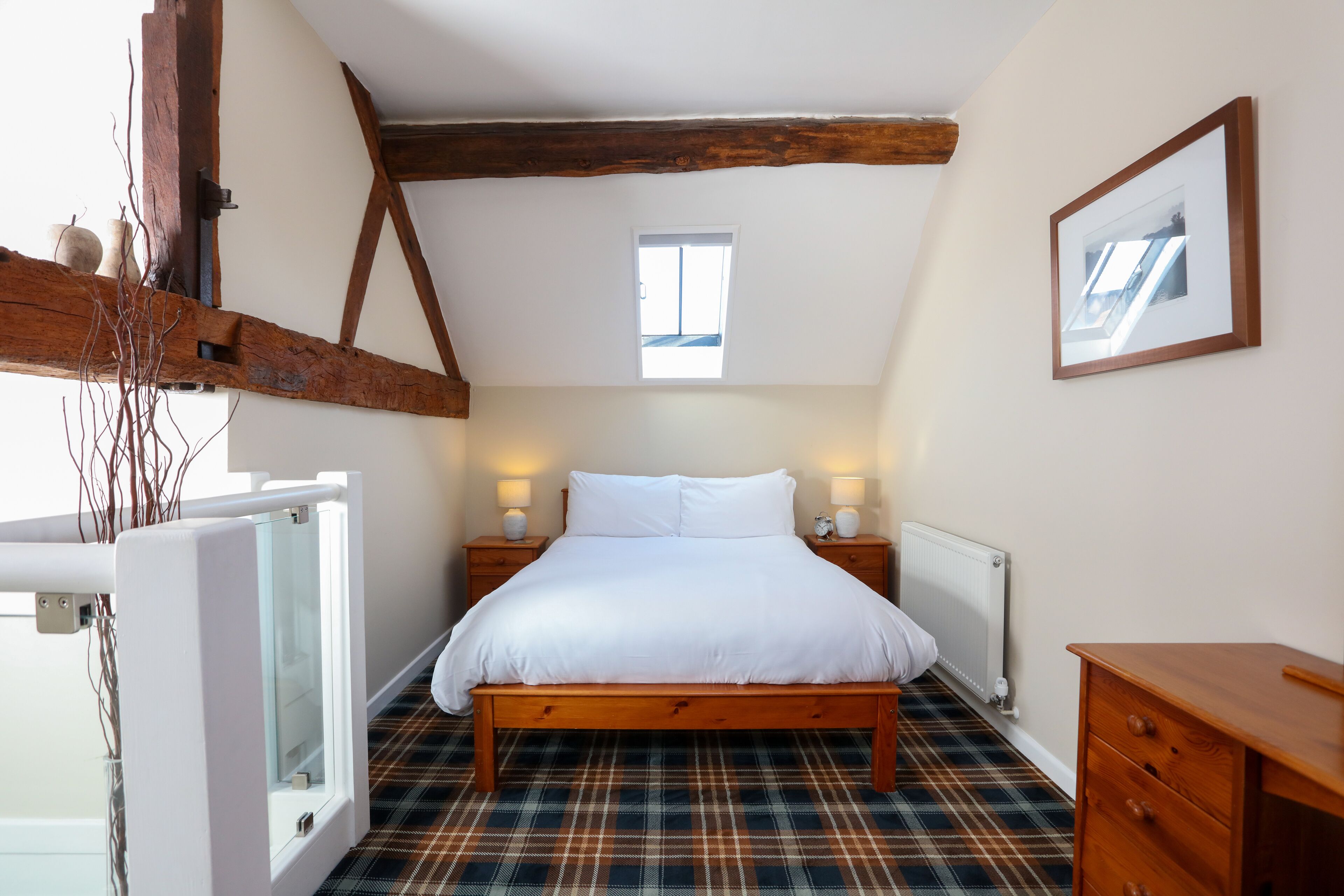 A bedroom with a wooden bed, plaid floor, a small window, and a framed picture on the wall.