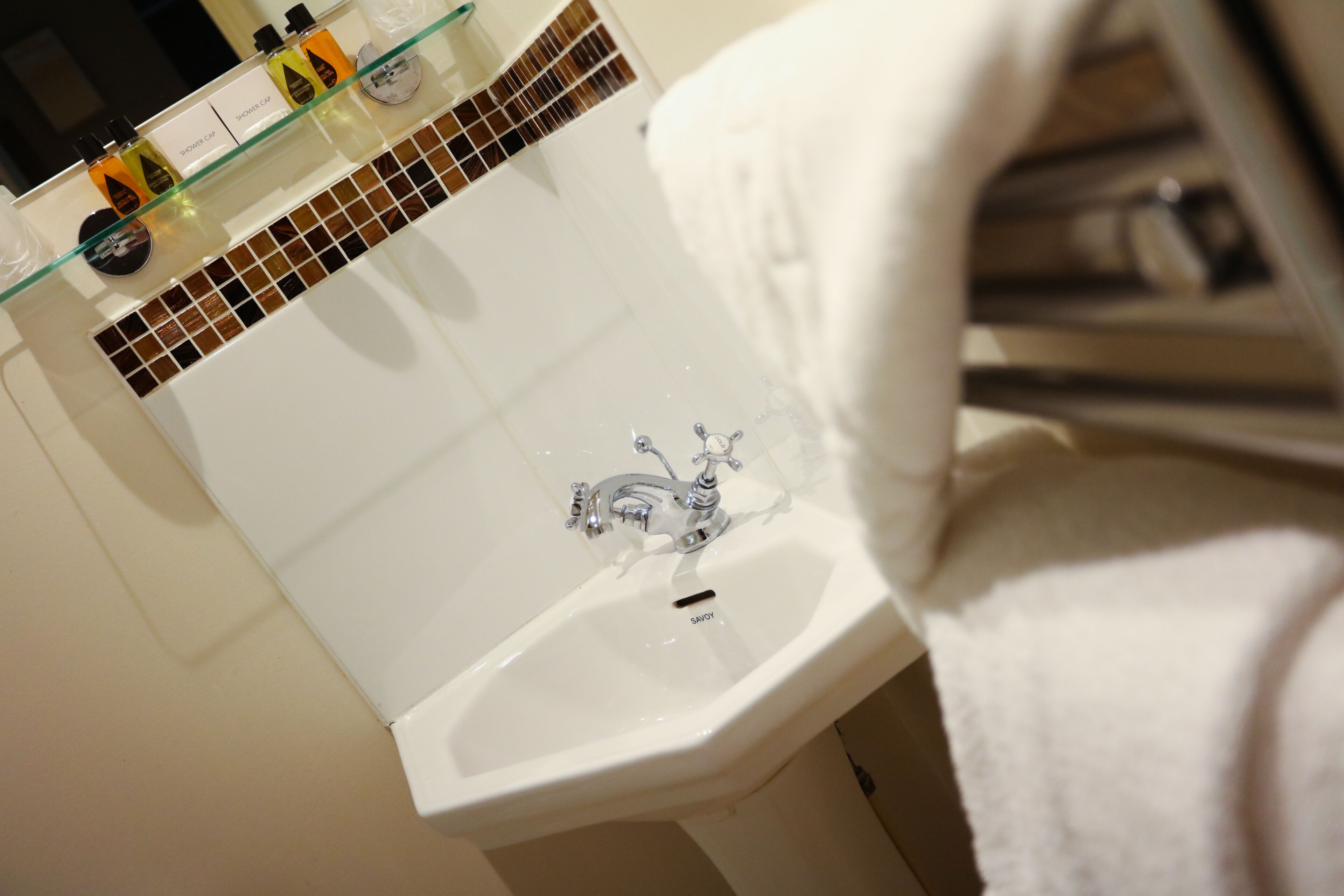 A bathroom with a white sink, a glass shelf with toiletries, and a towel hanging on a rack.
