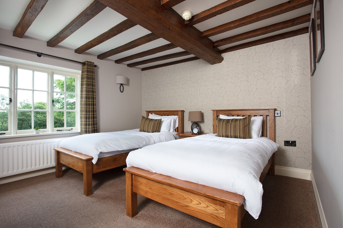 A bedroom with two wooden beds, a window with curtains, a wall-mounted lamp, and a radiator.