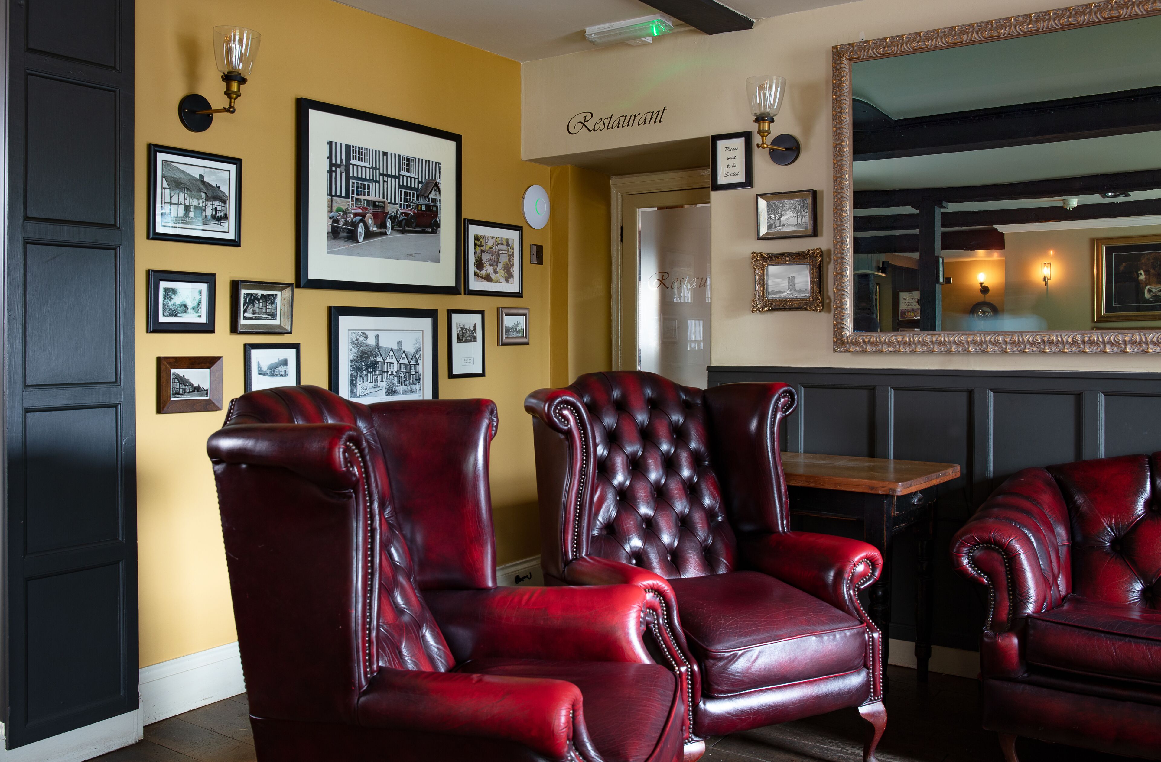 A restaurant interior with red leather chairs, framed pictures on the wall, and a mirror above the seating area.