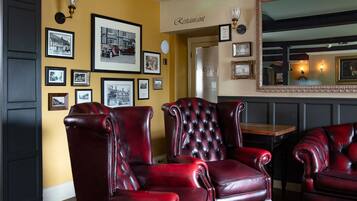 A restaurant interior with red leather chairs, framed pictures on the wall, and a mirror above the seating area.