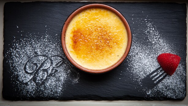 A dessert in a bowl on a slate board with powdered sugar and a strawberry. - Broom Hall Inn (Alcester)