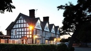 A Tudor-style building with multiple chimneys and a well-lit facade. - Broom Hall Inn (Alcester)