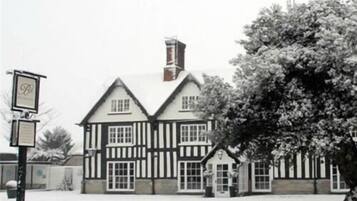 A traditional Tudor-style building with a symmetrical facade, multiple chimneys, and a prominent entrance with a door and windows.