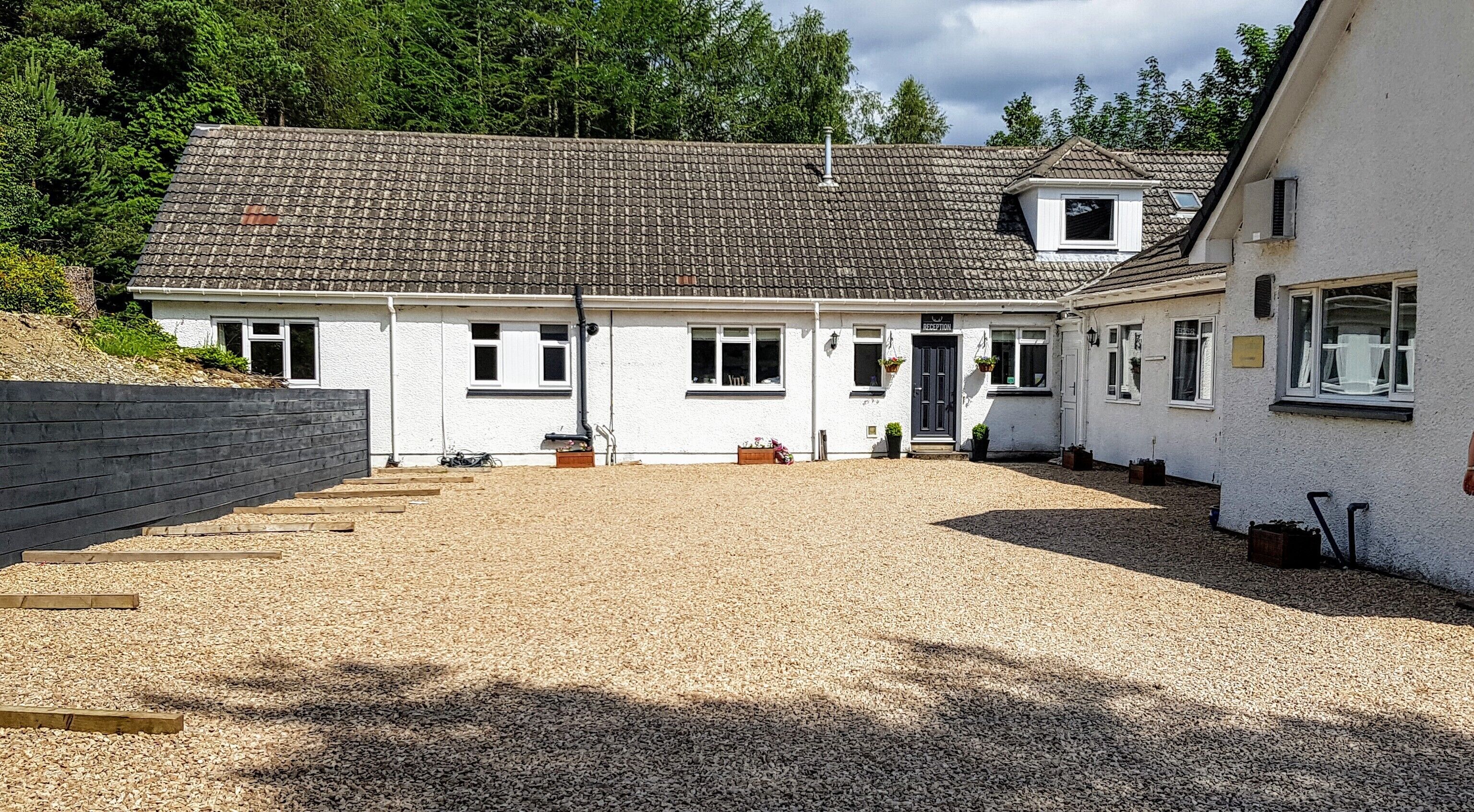 A white building with a tiled roof, a gravel driveway, and a wooden fence.