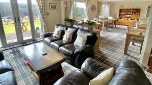 A spacious living room with a large black leather sofa, a wooden coffee table, and a dining area with a wooden table and chairs.