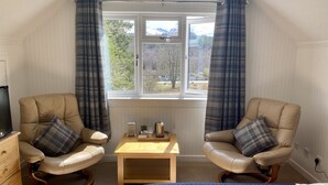 A room with two leather chairs, a wooden table, a bed, and a window with curtains.