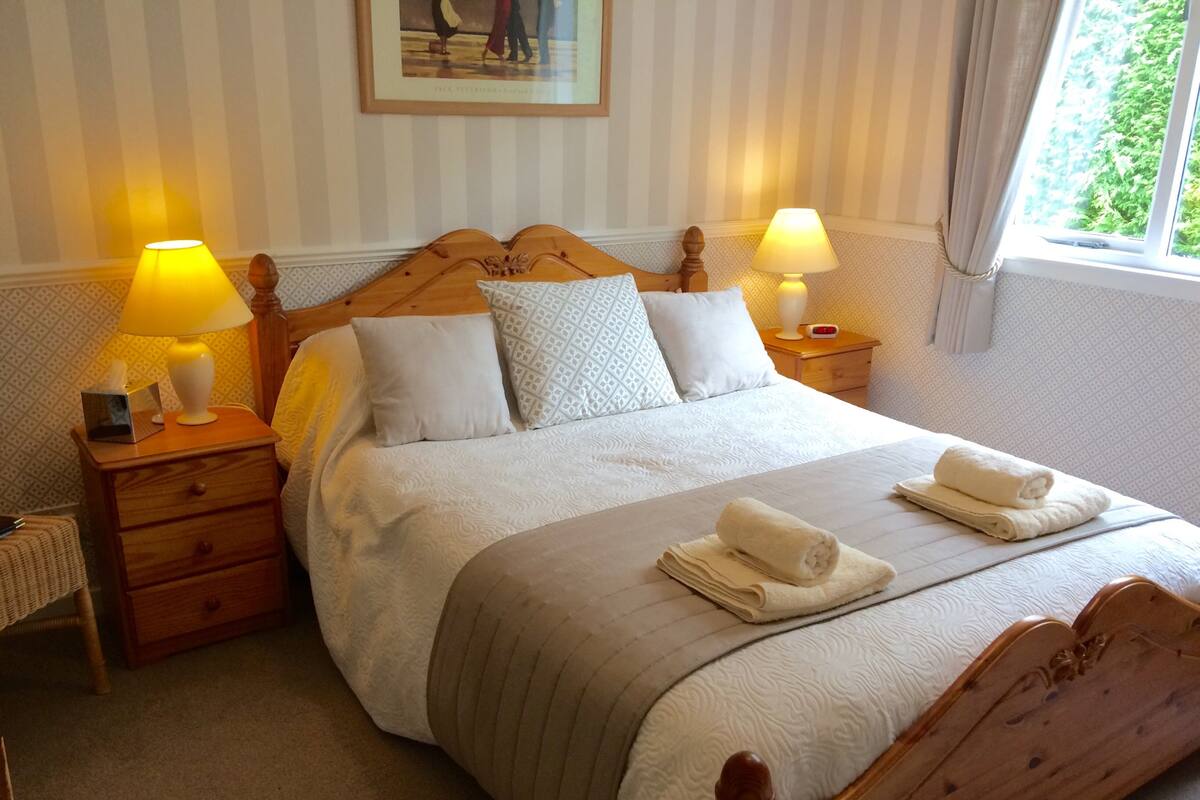 Ein ordentlich bezogenes Bett mit einem Holz-Kopfteil, zwei Nachttische mit Lampen und ein Bild an der Wand.