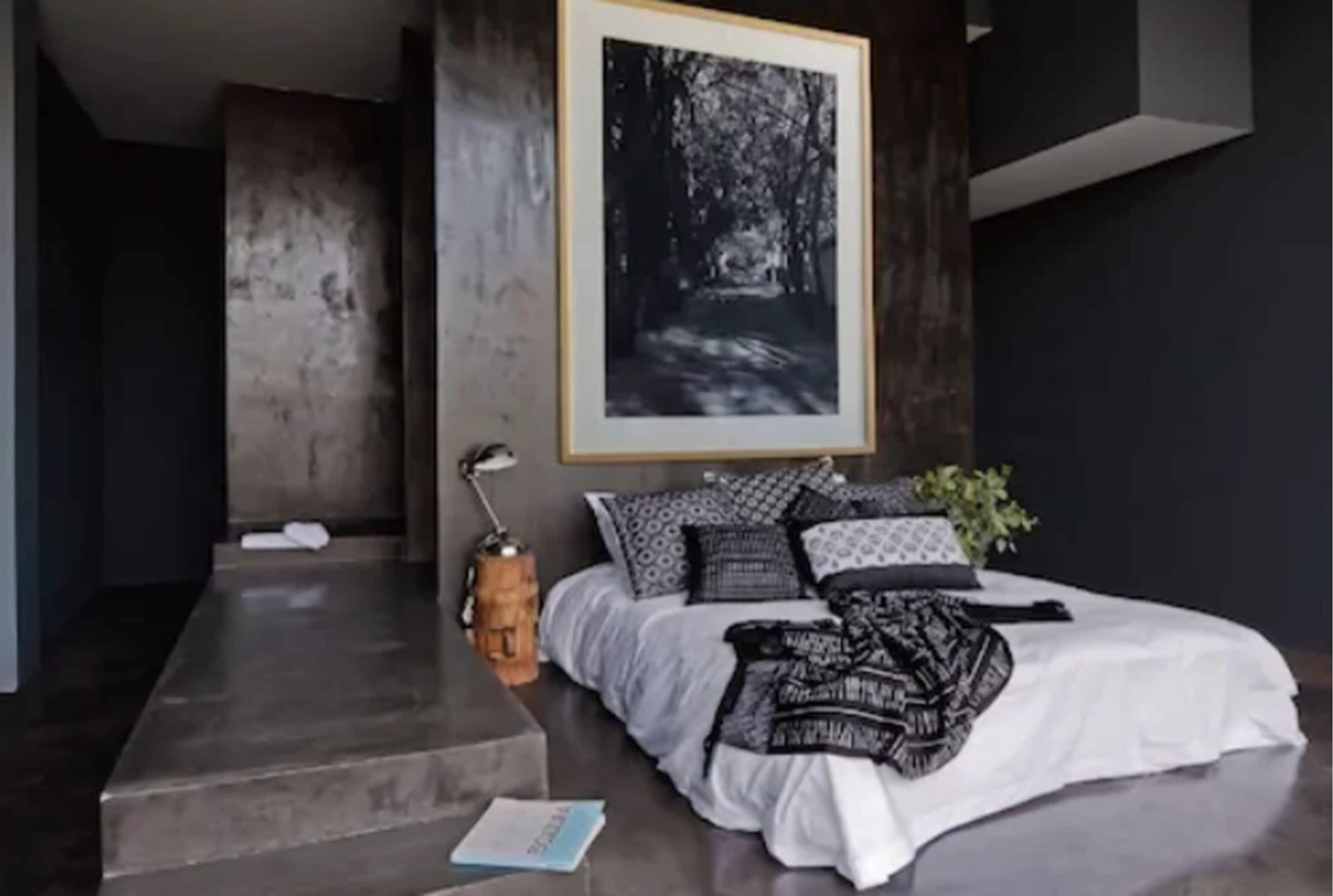 Un dormitorio con una cama, un cuadro en la pared, una mesita de noche y una escalera.
