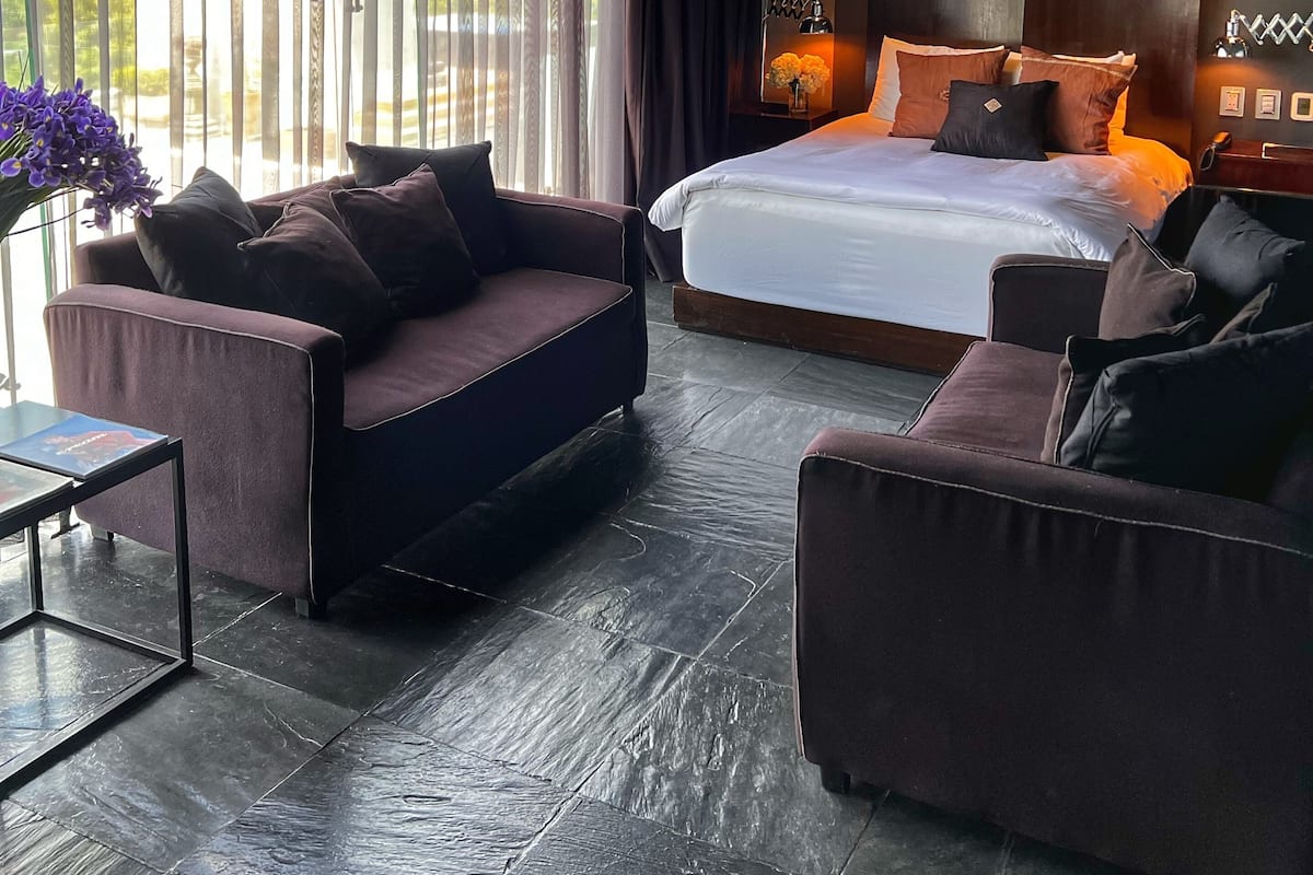 A modern bedroom with a large bed, dark walls, and a view through sheer curtains.