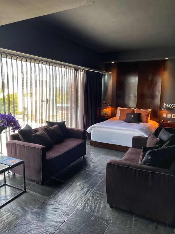 A modern bedroom with a large bed, dark walls, and a view through sheer curtains.