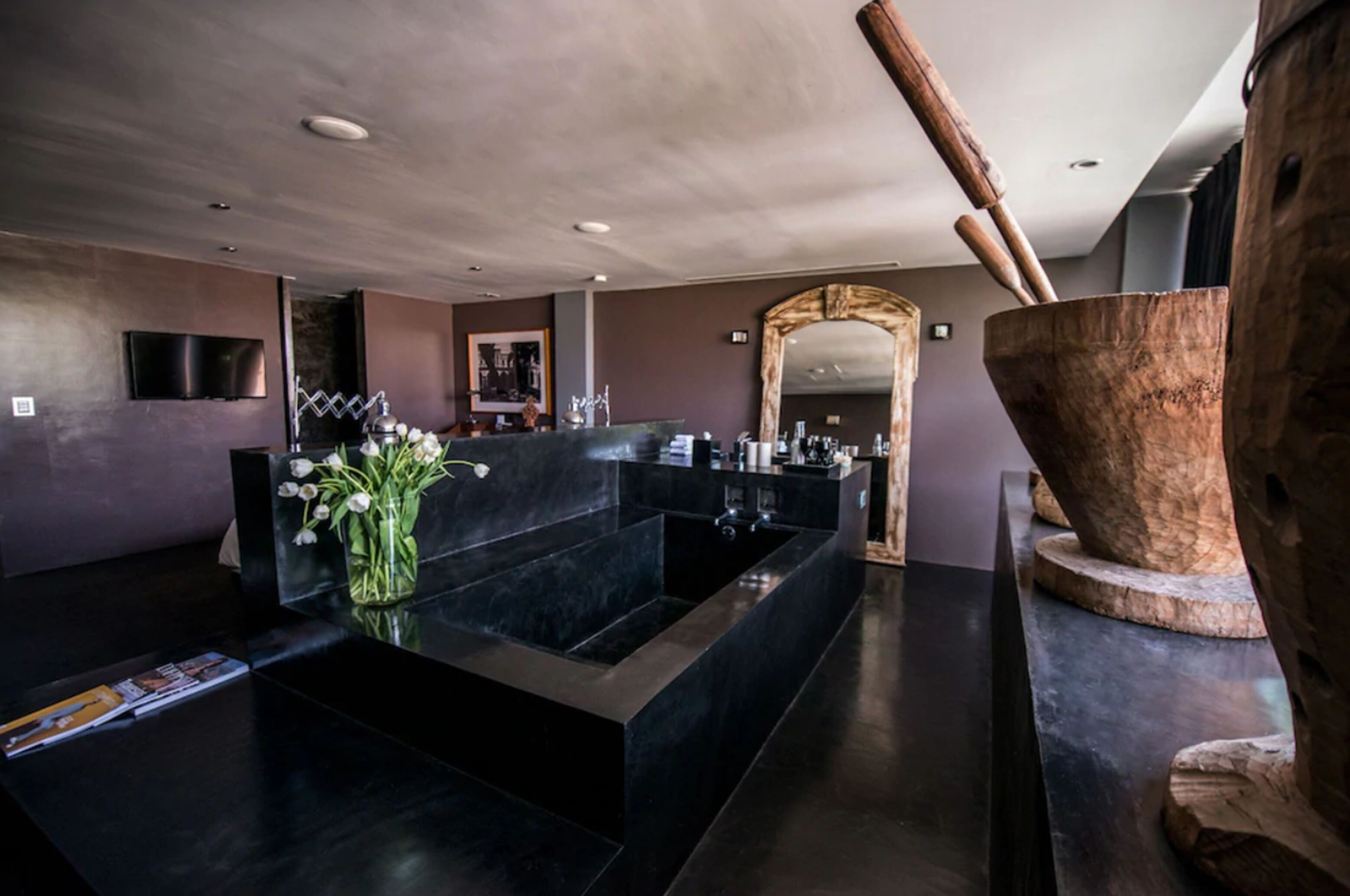 Un baño moderno con un lavabo negro grande, una bañera de madera y un espejo.